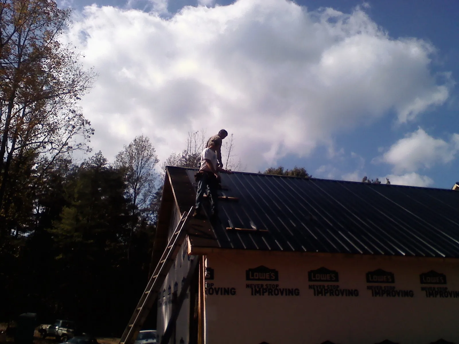 Roofer fastening dark metal panels high against a cloudy sky, from a Roof Inspection job in Cameron