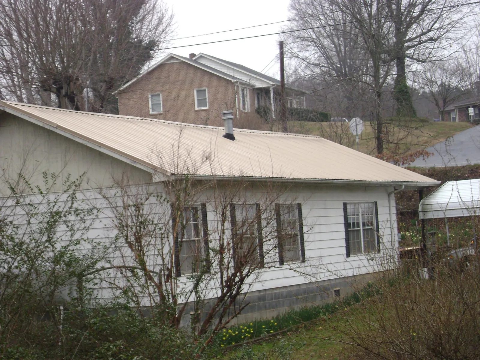 Tan metal roof on a white sided house set into a hillside — Commercial Roofing by Roofing Brothers in Cameron
