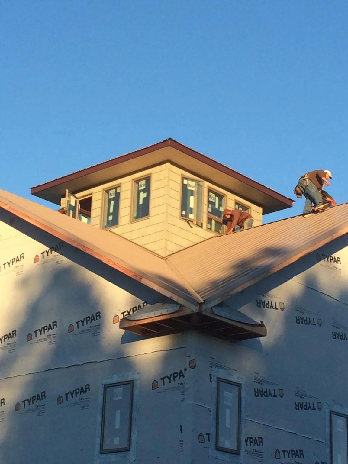 Roofers working around a rooftop cupola on a new metal roof at sunset — Roof Waterproofing in Cameron by Roofing Brothers